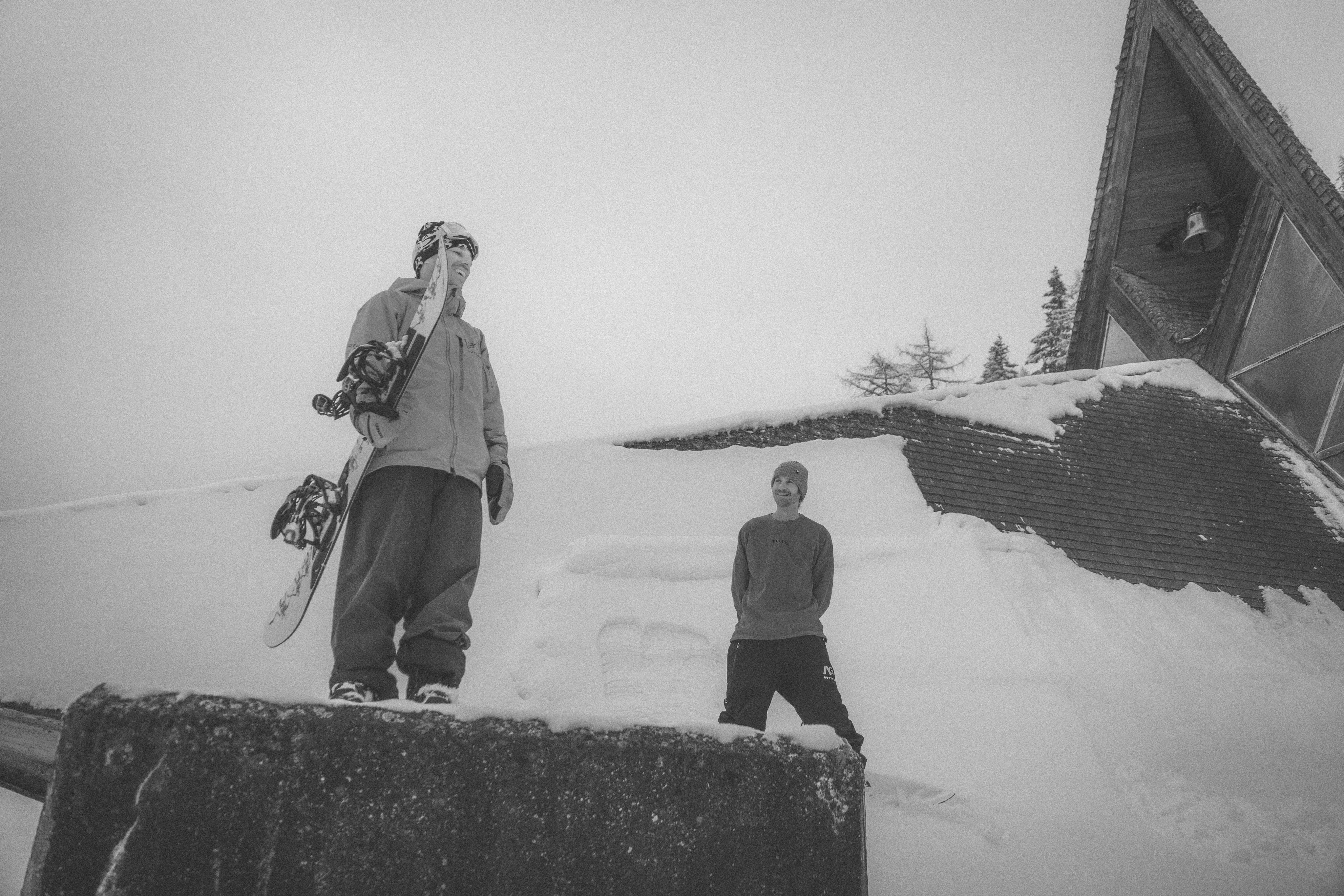 Snowboarder carrying gear outside a mountain hut